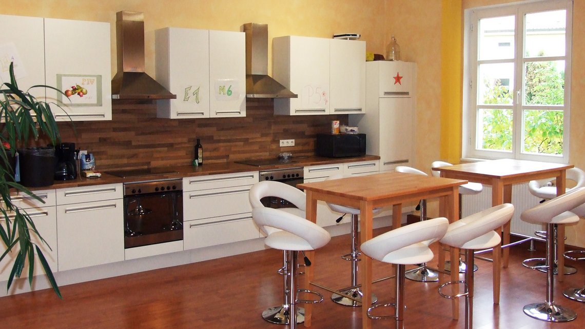 Offene Küche mit Theke und weißen Stühlen in der Kybalion Einrichtung