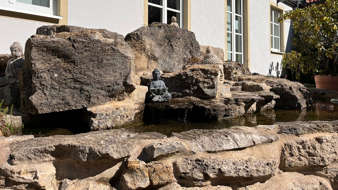 Natursteinbrunnen mit Wasserlauf vor dem Gebäude