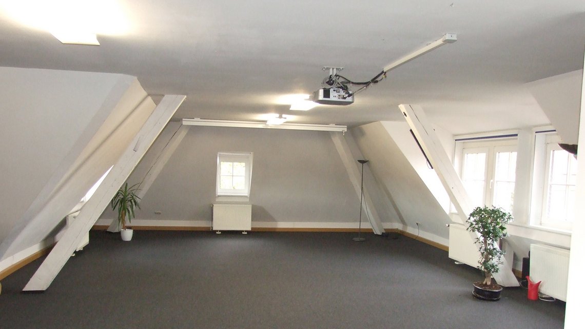 Unterrichtsraum im Dachgeschoss mit Leinwand und Fensterfront in der Kybalion Schule