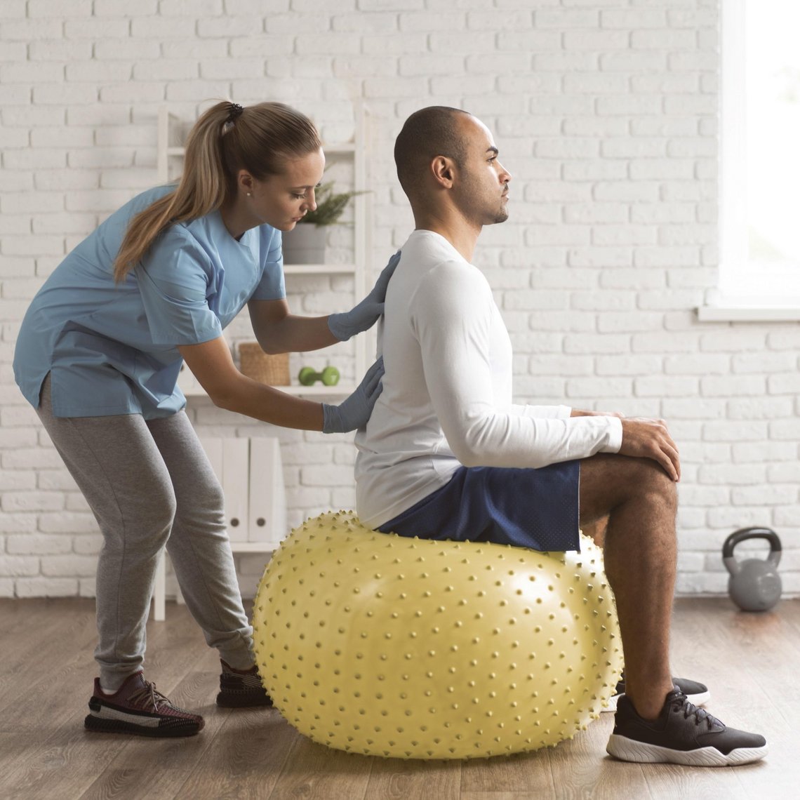 Therapeutin zeigt Kräftigungsübung für den Rücken mit Gymnastikball