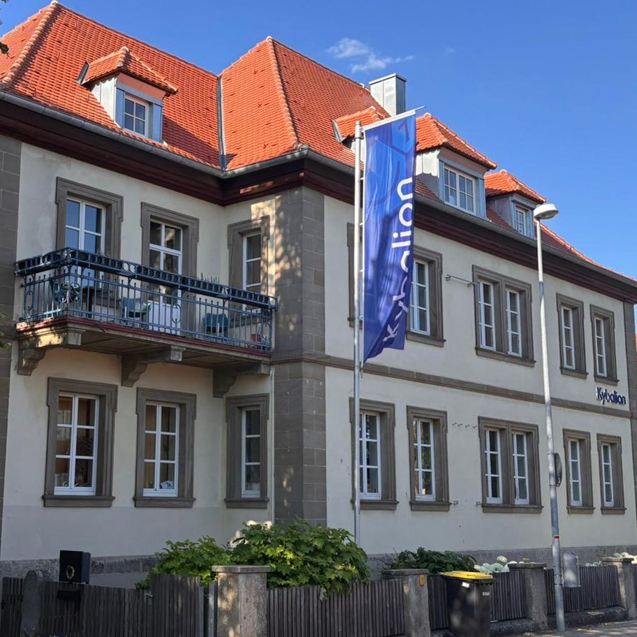 Kybalion Schulgebäude mit Fahne und Gartenbereich vor dem Eingang