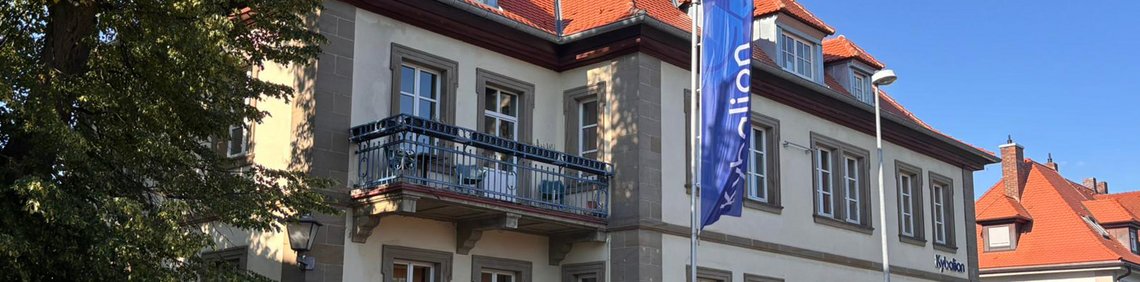 Kybalion Schulgebäude mit Fahne und Gartenbereich vor dem Eingang