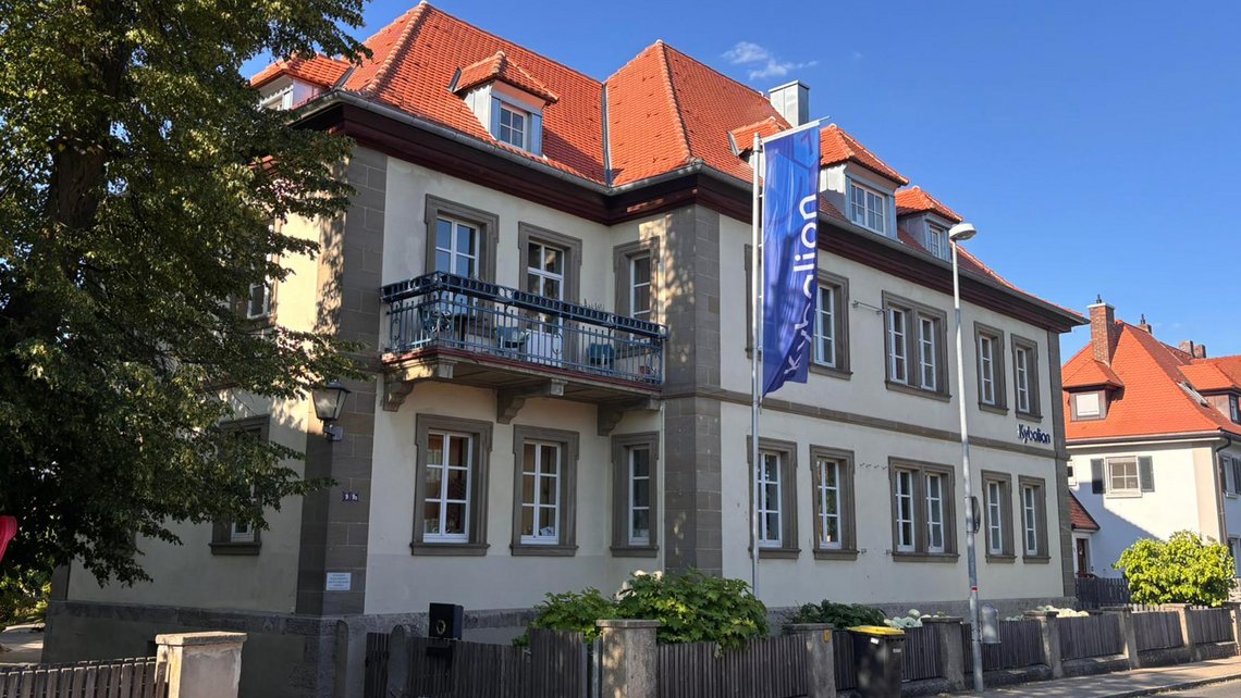 Kybalion Schulgebäude mit Fahne und Gartenbereich vor dem Eingang